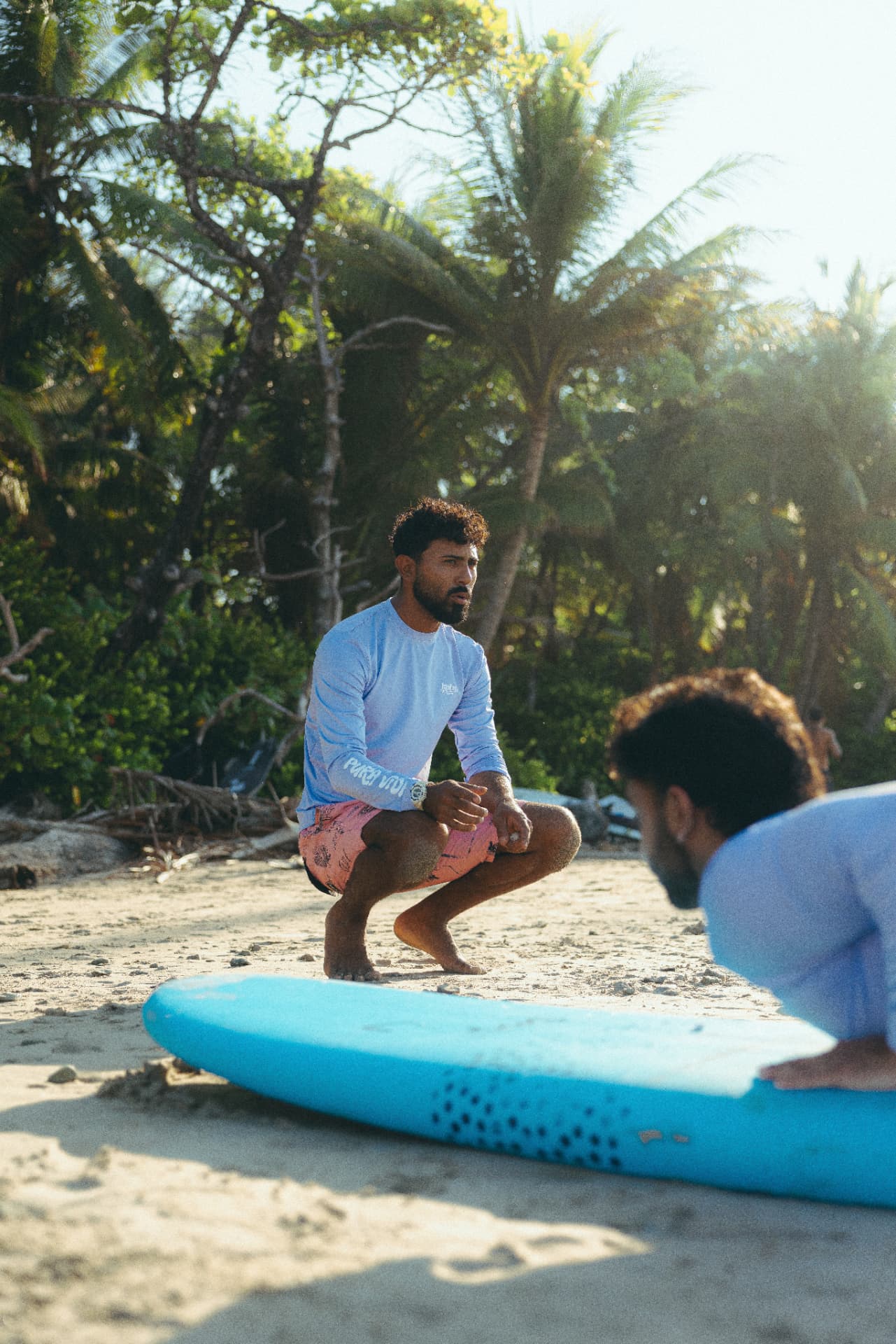 Coach watching a surfer practise her pop-up on a blue board on the sand