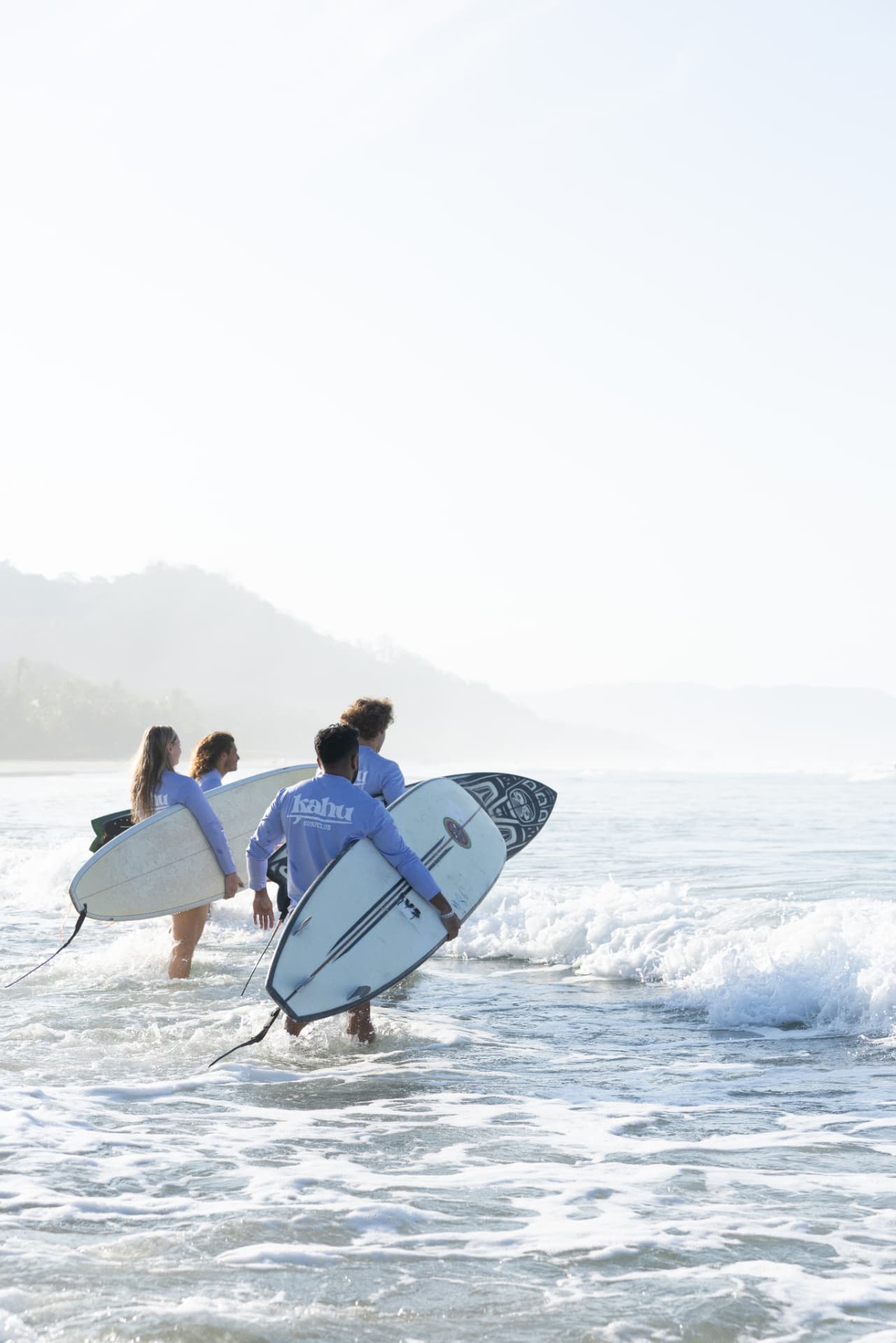 Four surfers carrying their boards as they wade through the shallows out to the lineup