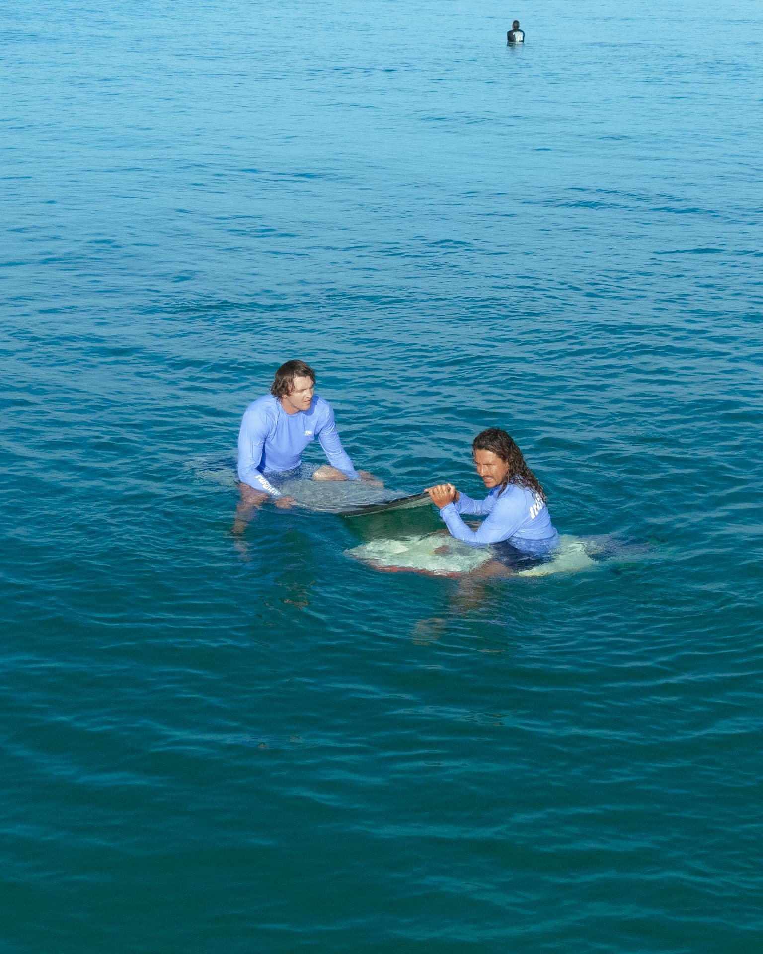 Two surfers floating on their boards in deep blue water, seen from above